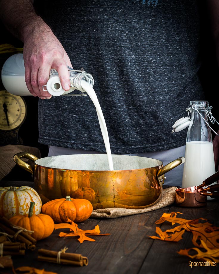 Pouring milk in a cooper pot. The scene is decorated with fall decor. Spoonabilities.com