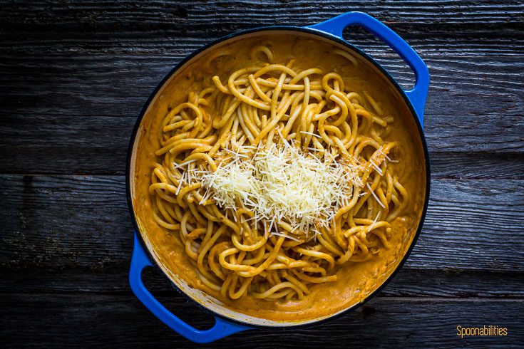 Pasta mixed with pumpkin pasta sauce with Parmesan cheese in a blue cast iron pan. Spoonabilities.com