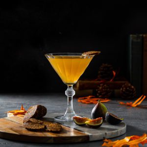 Recipe of a Fig Vodka Martini in a vintage cocktail glass on top of a serving board with fall decoration, fresh fig and vegan fig salami. available at spoonabilities.com