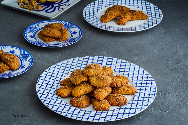 White and blue plate with Greek Christmas cookies and three more plates in the background with cookies. Spoonabilities.com