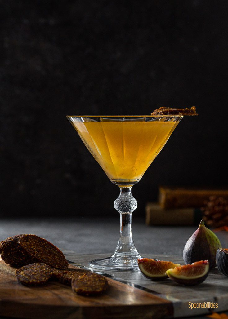 Fig Jam Vodka Martini in a close up photo with fresh fig and fig salami around the cocktail glass on a wooden/marble board. 