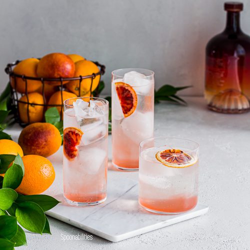 Three Blood Orange Vodka Sodas on a marble cutting board with bottle of Salerno in background