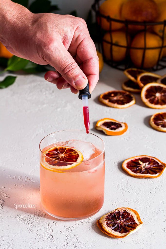 Eye dropper of blood orange juice giving color to a blood orange vodka soda cocktail