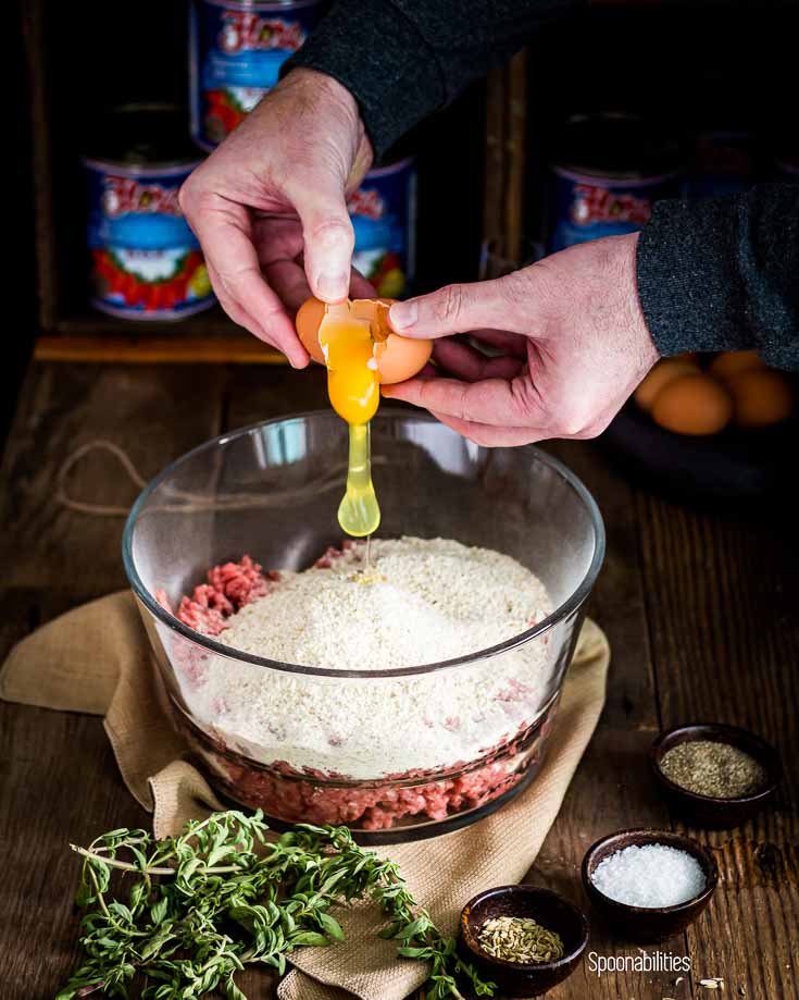 Ingredients in the mixing bowl and two hands cracking a egg over the mixture. Spoonabilities.com