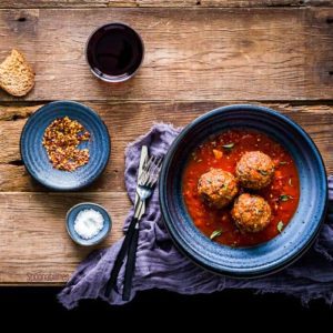 Three meatballs in a blue bowl with two small saucers with condiments on the left side. Spoonabilities.com