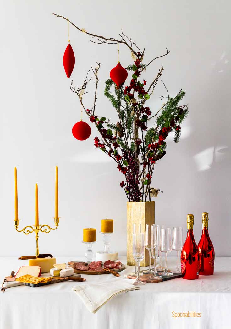Holiday table decorated with Pillar Candles, drinks, food & flowers in a table with white tablecloth. Spoonabilities.com