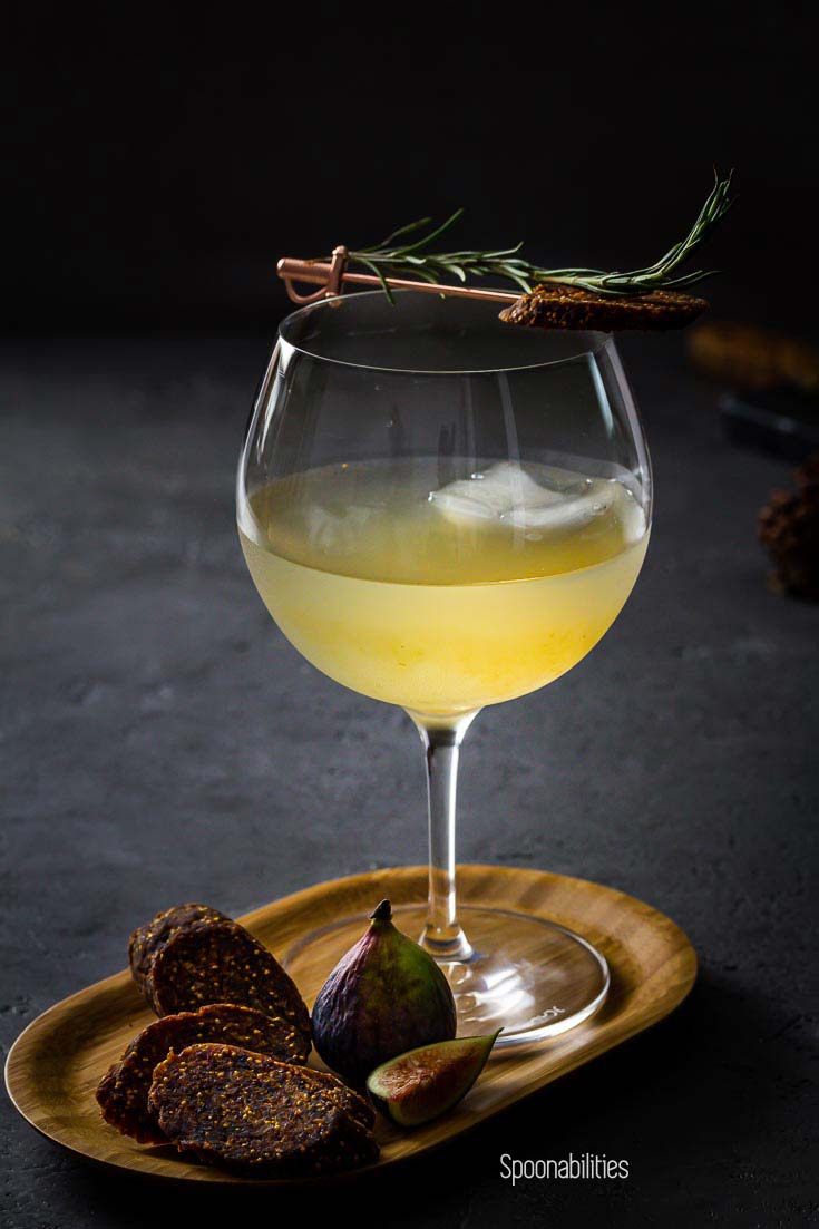 Closeup photo of Bloomsbury Garden Cocktail with large ice cube, and rosemary and fig salami garnish