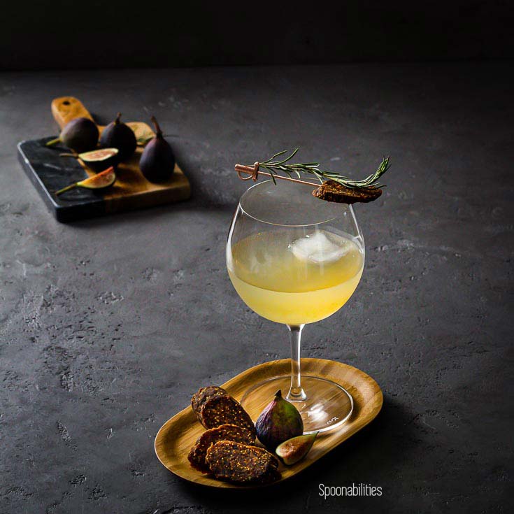 Glass of Rosemary Gin, Elderflower & Fig Tonic on a small wood tray with figs