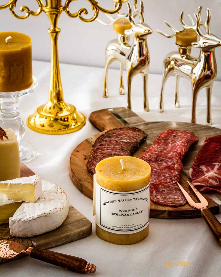 Beeswax pillar candles in a table with white tablecloth and in the background a board with charcuterie. Spoonabilities.com