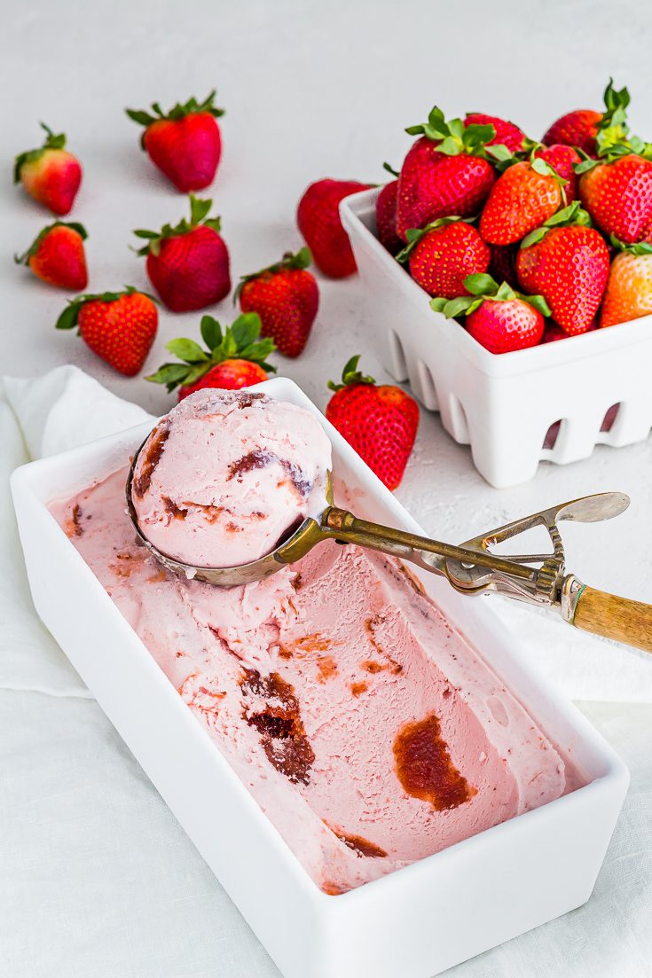 Old fashion ice cream scoop full of strawberry ice cream and white basket of fresh strawberries