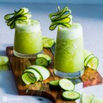 Two glasses on a wooden board with cucumber margarita slush. Garnished with shaved cucumbers. Recipe at Spoonabilities.com