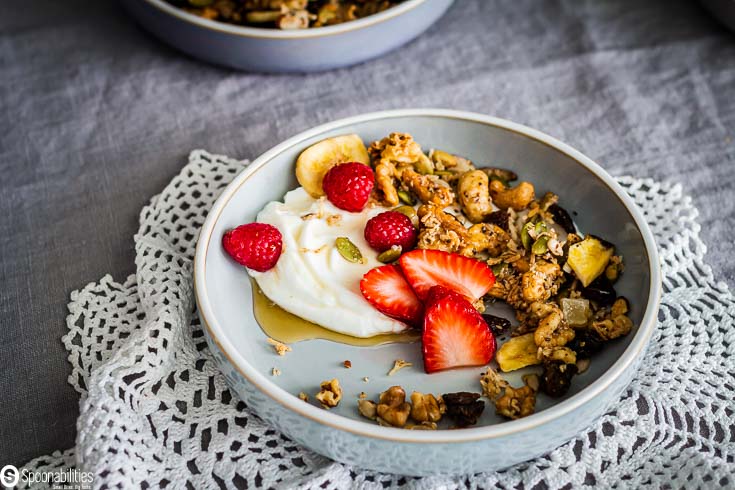 Light blue bowl with Greek yogurt, grain-free granola with strawberries and raspberry with a drizzle of maple syrup. Recipe at Spoonabilities.com