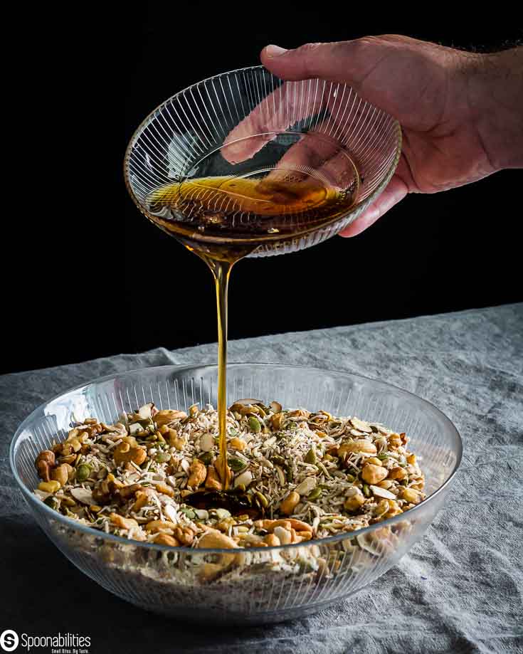 Gluten-Free granola mixture in a large glass bowl and a hand pouring the liquid mixture into the large bowl. Recipe available at Spoonabilities.com