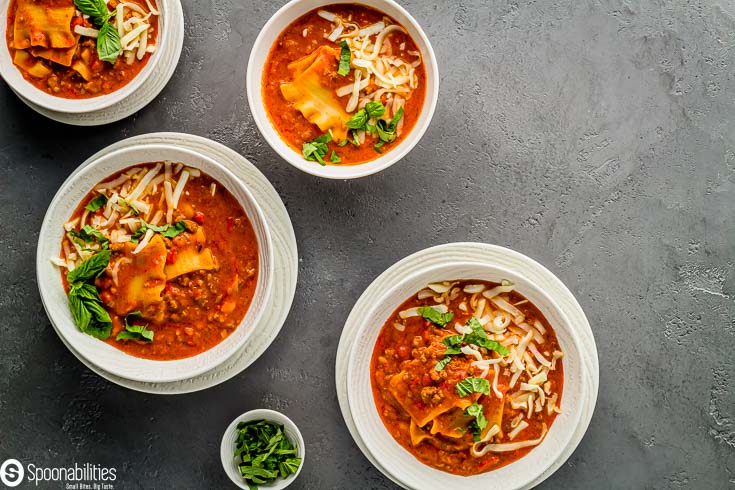 Four white bowls with lasagna soup and garnished with basil and mozzarella cheese. Recipe at Spoonabilities.com