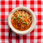 Red and white tablecloth and a white bowl in the center with Lasagna Soup. Recipe at Spoonabilities.com