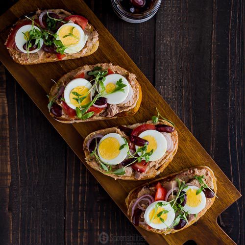 Square photo with an overhead shoot for the Tuna Nicoise Crostini using Anise Marinated Kalamata Olives. Available at Spoonabilities.com