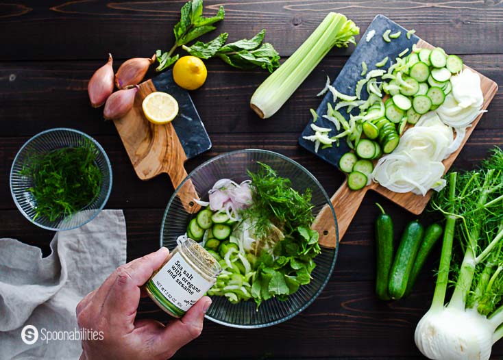 The slaw ingredients in a glass bowl and adding the sea salt with oregano and sesame. Recipe at Spoonabilities.com