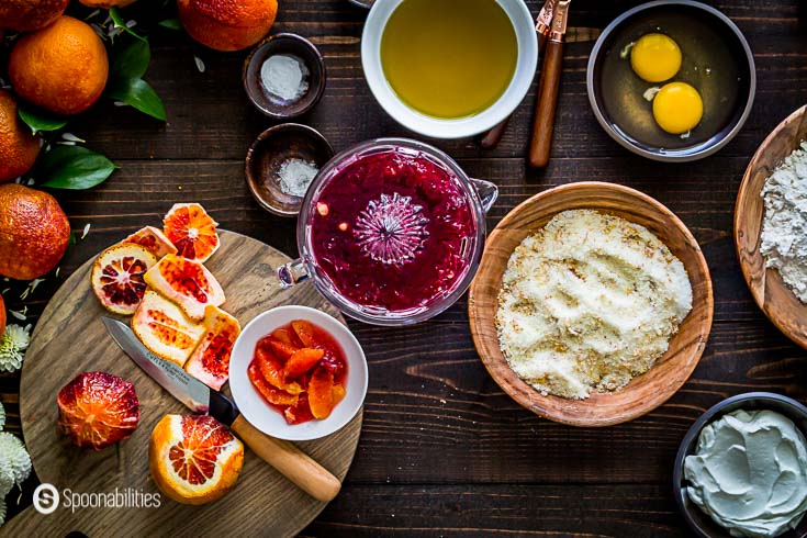 Wooden table with some of the blood orange cake ingredients but in this step we squeeze the orange. More details at Spoonabilities.com