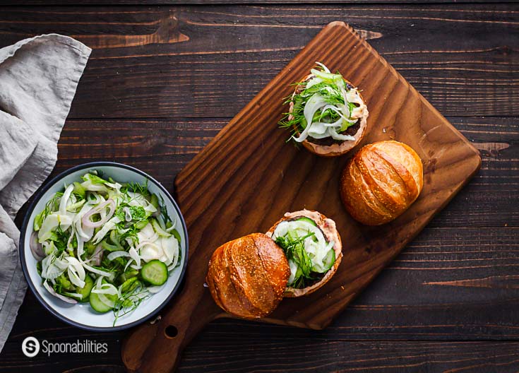 Four Mediterranean lamb burger with a side of fennel, cucumber & celery slaw on a wooden cutting board. Spoonabilities.com