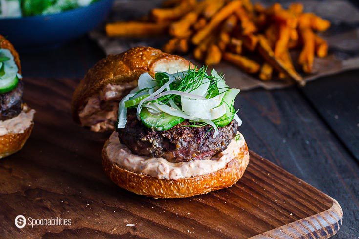 Close up of the Spiced Lamb Burger topped with a Celery, Cucumber & Fennel Slaw on a wooden board. Recipe details at Spoonabilities.com