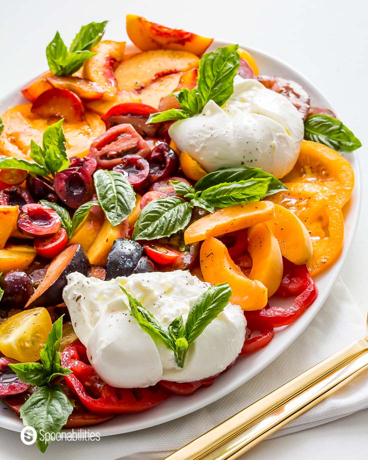Photo of the caprese salad with stone fruits on a white oval plate with golden serving ware. Recipe at Spoonabilities.com