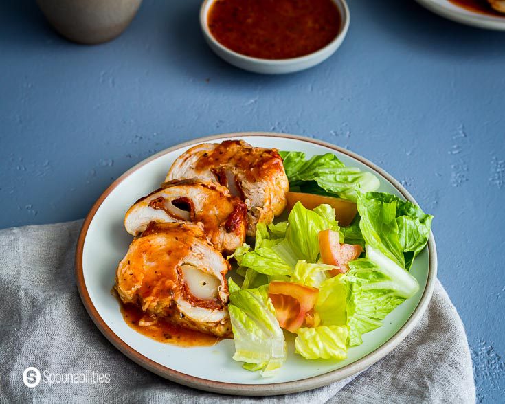 Round plate with three pieces of pizza stuffed chicken with a side of salad of lettuce and tomatoes. Recipe at Spoonabilities.com