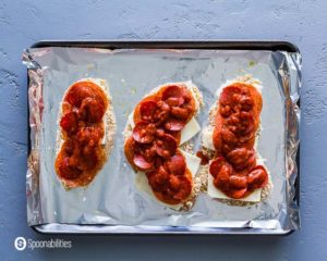 Breaded chicken Parmesan topped with mozzarella cheese,pepperonis, and pizza sauce in a baking tray, before they go to the oven. Recipe at Spoonabilities.com