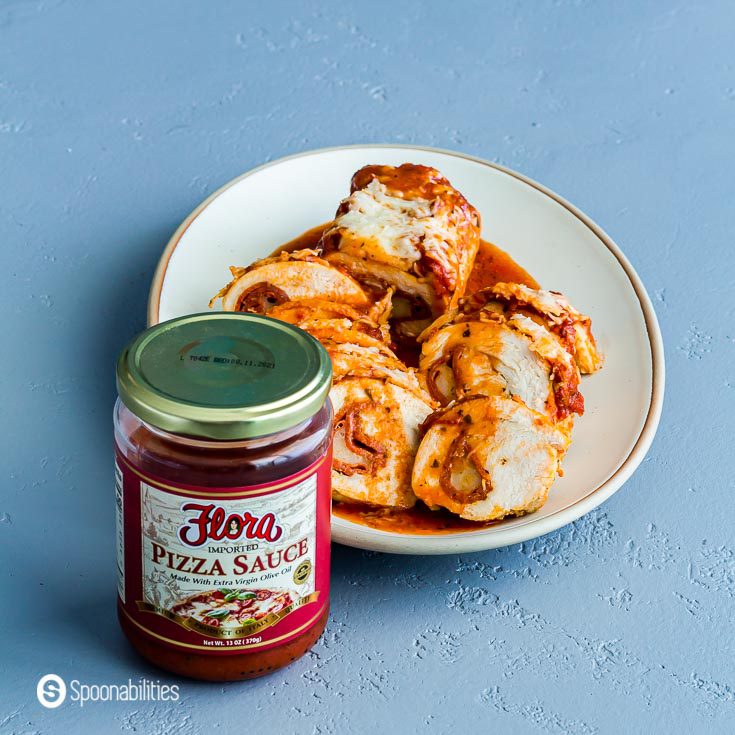 A jar of Pizza Sauce from Flora fine Foods and behind is an oval serving plate with the Cheesy Pepperoni Pizza Chicken. Recipe at Spoonabilities.com