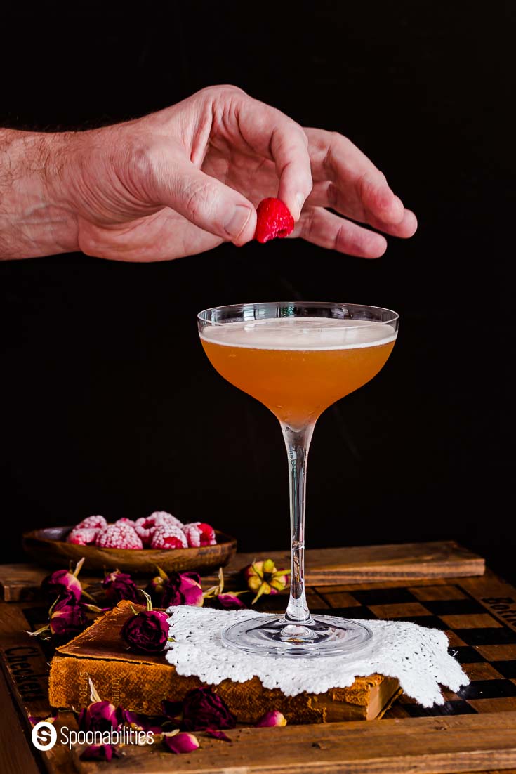 hand placing a fresh raspberry as a garnish on top of a french martini