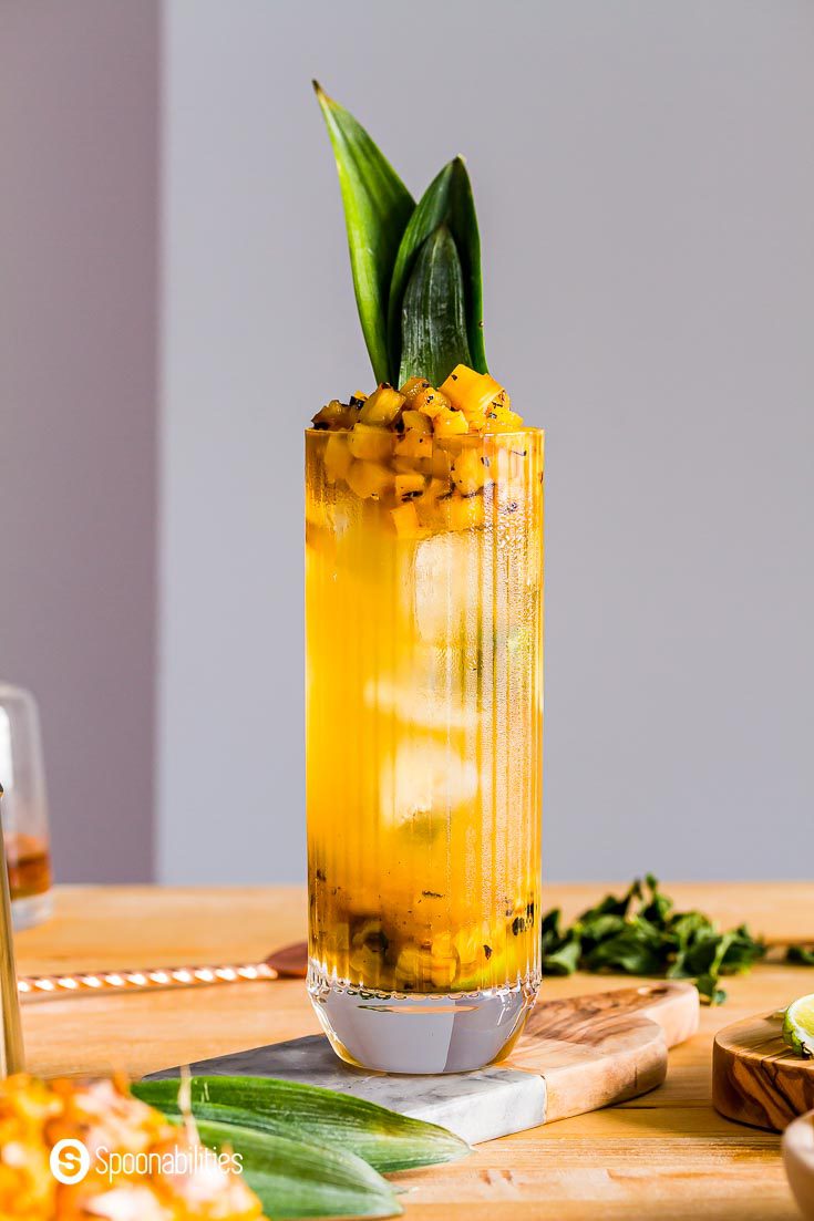 Close up photo with a pineapple mojito in the center of the photo on top of a wooden counter-top. Recipe at Spoonabilities.com