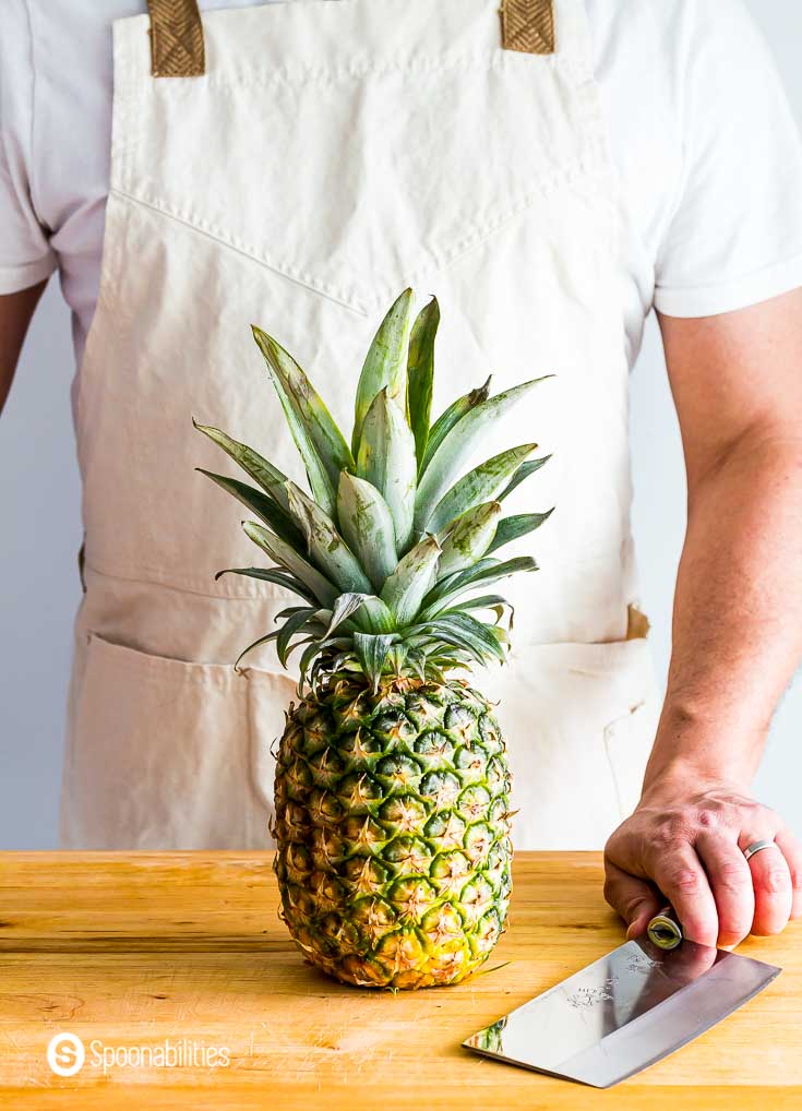 One pineapple on top of the counter top. Behind the pineapple is a guys with a knife, ready to cut the fruit. Recipe at spoonabilities.com
