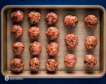 Baking tray with eighteen raw lamb meatballs mixed with fig salami. Recipe at Spoonabilities.com