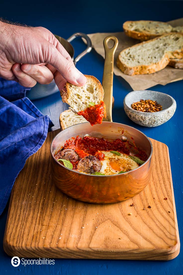 Soaking a piece of crusty bread into the roasted red pepper and tomato sauce from the shakshuka. Spoonabilities.com