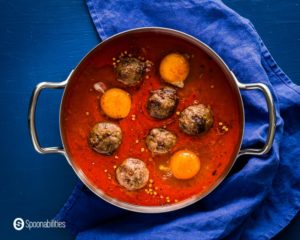 Medium saucepan with the Easy shakshuka before go to the oven. This saucepan has six lamb meatballs with three eggs. Recipe at Spoonabilities.com