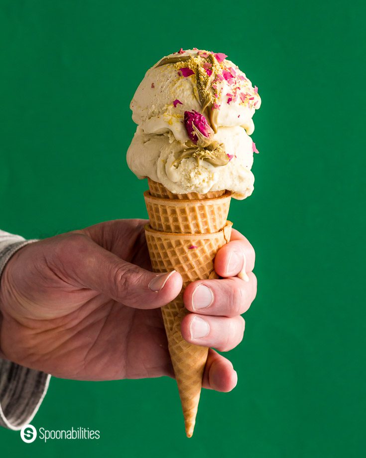 A hand holding a sugar cone with two scoops of Pistachio Ice cream with Rosewater & Saffron. Recipe at Spoonabilities.com