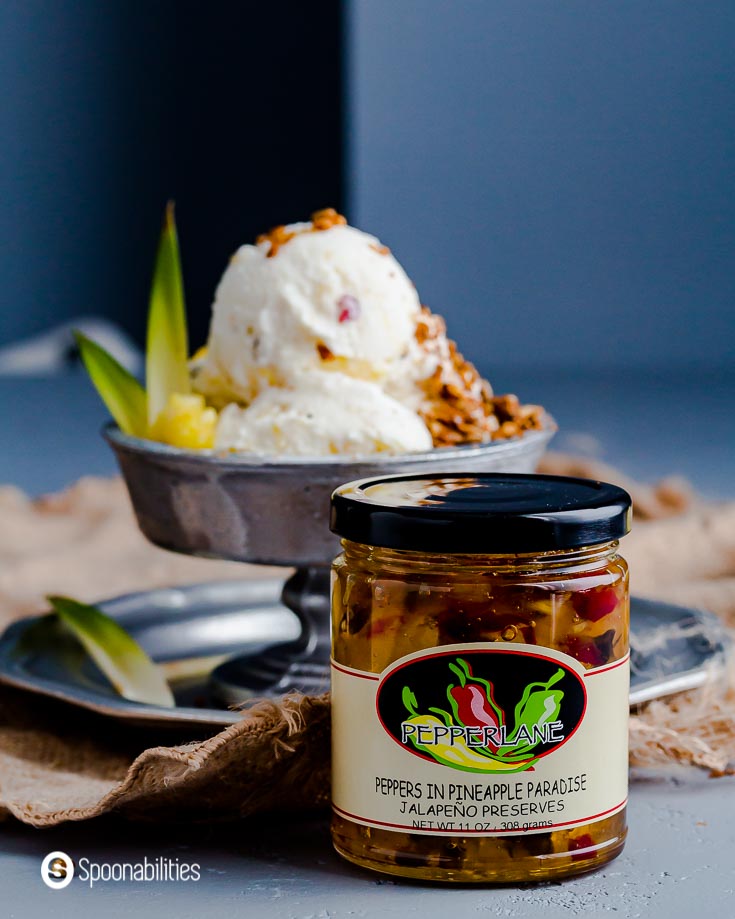 A jar of Peppers in Pineapple Paradise Jalapeno Preserves from pepperlane. In the background a metal ice cream bowl with pineapple jalapeno ice cream. recipe at Spoonabilities.com