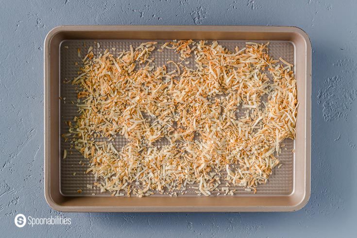 Toasted coconut flakes in a small baking tray. Recipe at Spoonabilities.com