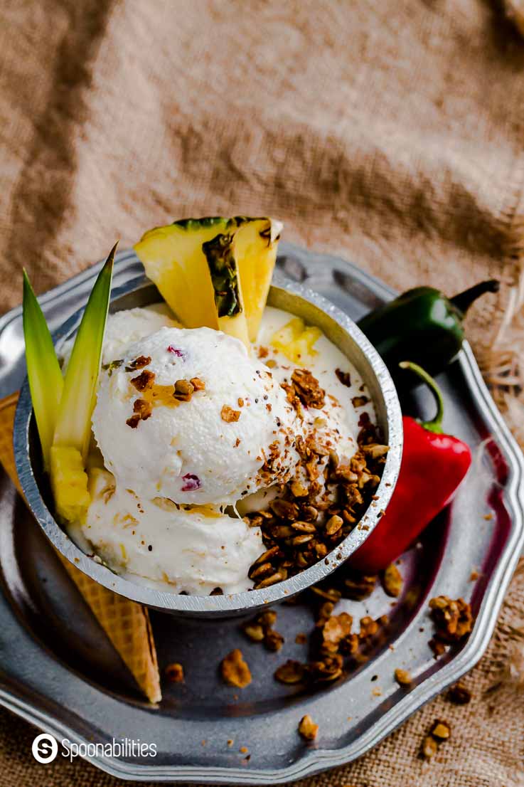 Close up of the pineapple ice cream with peppers. The ice cream is in a metal bowl with toppings like granola, fresh pineapple and pineapple spikes. Recipe at Spoonabilities.com