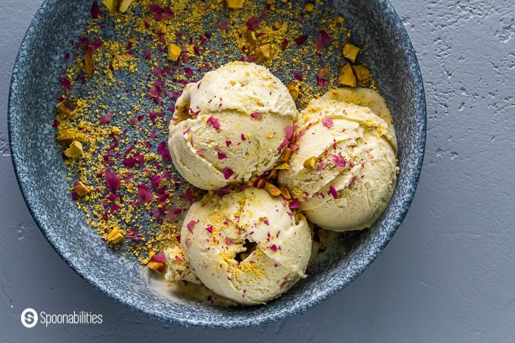 Three Pistachio ice cream in a blue bowl. Garnished with crushed rose petals and pistachios. Recipe at Spoonabilities.com