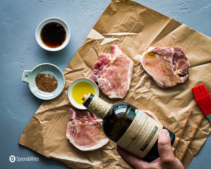 Pouring Greek olive oil Navarino Icons in a small bowl before brushing the four pork chops. Recipe at Spoonabilities.com