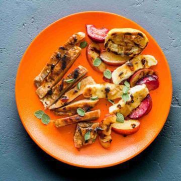 Orange plate with grilled pork chops, grilled plums, grilled Halloumi with fresh oregano leaves and some cherry ancho chili sauce. Recipe at Spoonabilities.com