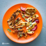 Orange plate with grilled pork chops, grilled plums, grilled Halloumi with fresh oregano leaves and some cherry ancho chili sauce. Recipe at Spoonabilities.com