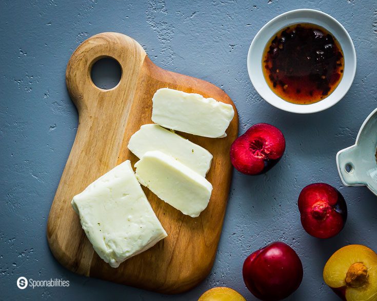 Cutting board with Halloumi cheese, plums and Cherry Ancho Chili Sauce. Recipe at Spoonabilities.com