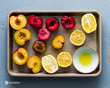 Baking tray with lemons, two color plums and olive oil in a small pinch bowl. Recipe at Spoonabilities.com