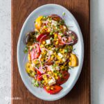 An oval pewter finish plate on top of a wooden board with Simple Heirloom Tomato Salad. Recipe at Spoonabilities.com