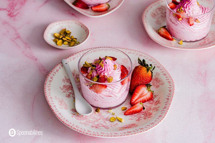 In the photo you will find two glasses with a mousse made out of strawberries. The glasses are on top of a small pink/white plate and garnished with chopped berries and nuts. Recipe at Spoonabilities.com