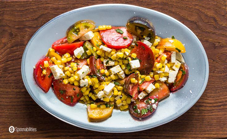 Close up photo of this salad with Heirloom tomatoes, feta cheese, microgreens, red onions, and corn. Recipe at Spoonabilities.com