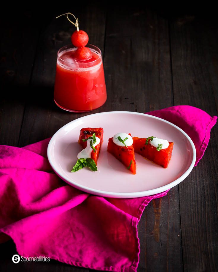 Pink round plate on top of a pink napkin with three wedges of grilled watermelon with Greek yogurt lime crema. Recipe at Spoonabilities.com