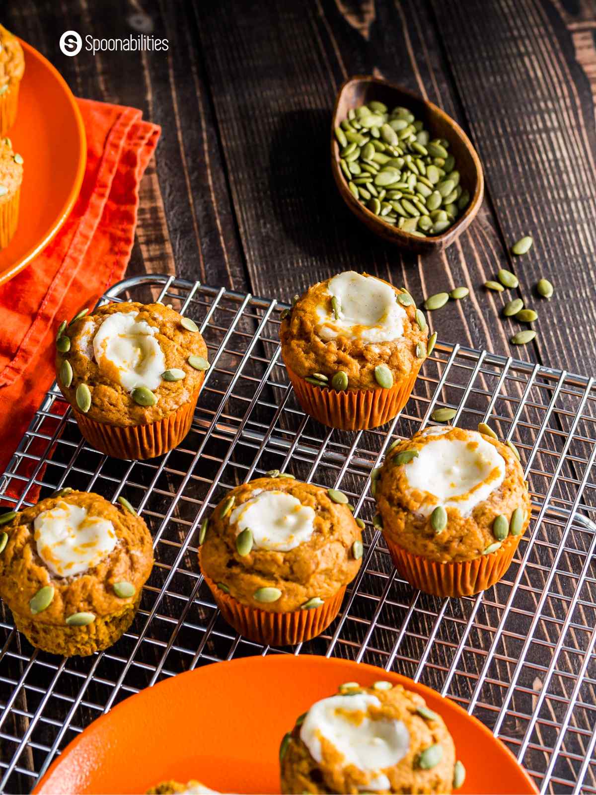 A bunch of freshly-baked pumpkin muffins on a cooling rack with some pumpkin seeds in the background