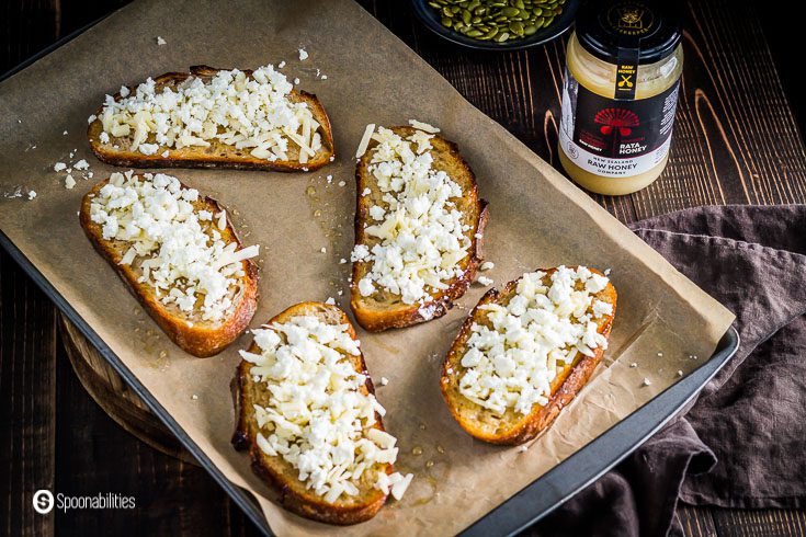 A baking tray with five Feta Honey Toast ready to go into the oven for 10 minutes. The toasted was brushed with honey, sprinkle some cheddar cheese, and feta cheese. Recipe at Spoonabilities.com